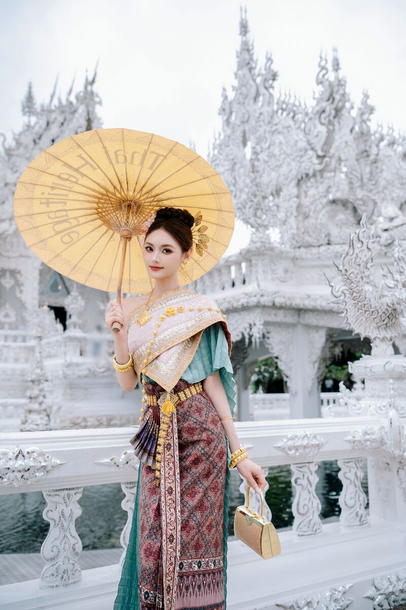 Woman in a Thai shawl and patterned skirt holding a Thai Heritage paper parasol at the White Temple in Chiang Rai
