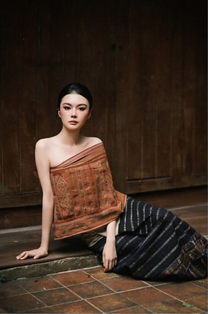 ชุดน้ำตาลใบชา: เสื้อผ้าทอสีสนิมกับผ้านุ่งลายริ้วสีคราม นั่งบนพื้นกระเบื้องดินเผา