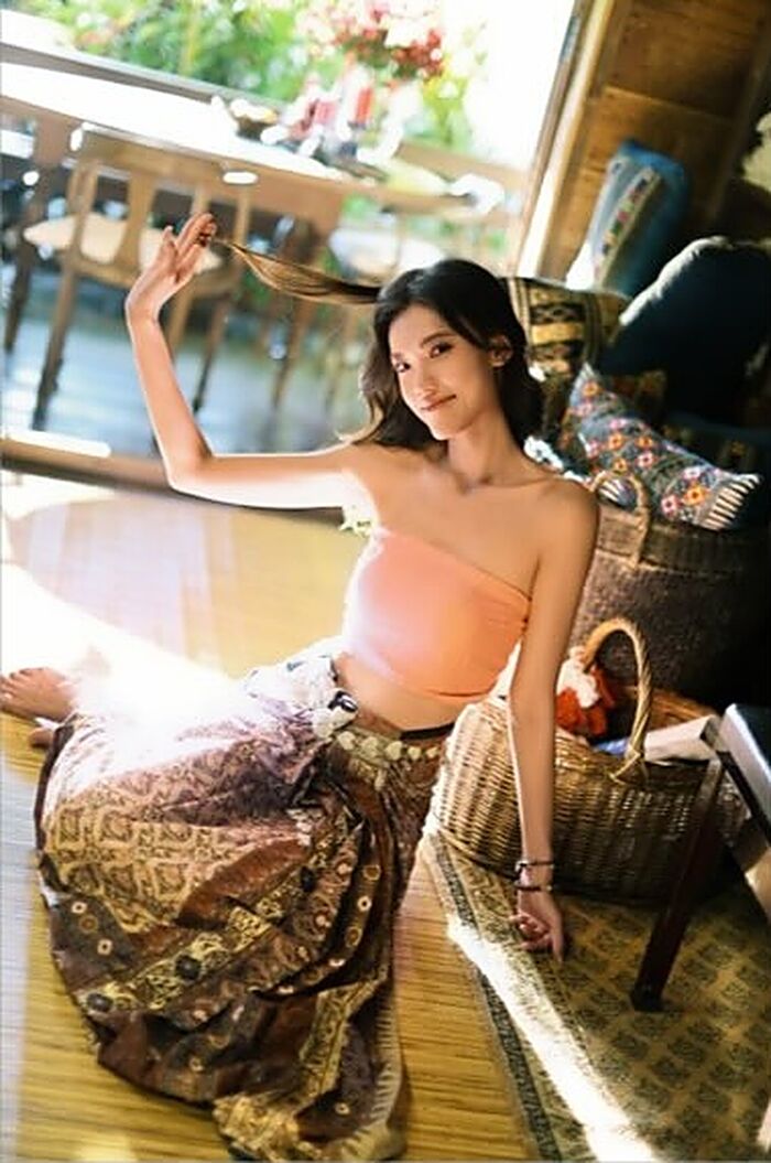 ชุดเม็ดมะขาม: เสื้อสีพีชกับผ้านุ่งสีน้ำตาลทอง นั่งในห้องที่มีแดดส่อง ข้างตะกร้าสาน