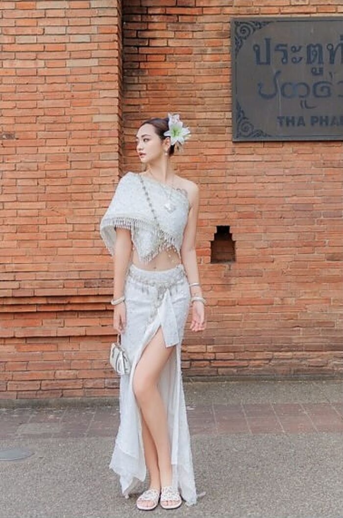 ชุดแสงจันทร์: เสื้อและผ้านุ่งปักเลื่อมสีขาวเงิน ยืนหน้ากำแพงอิฐ