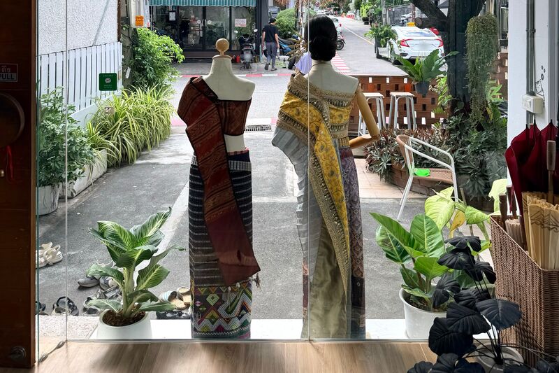 从店内透过橱窗往外看：两个着装人台的背影、几盆绿植，以及窗外的巷子。