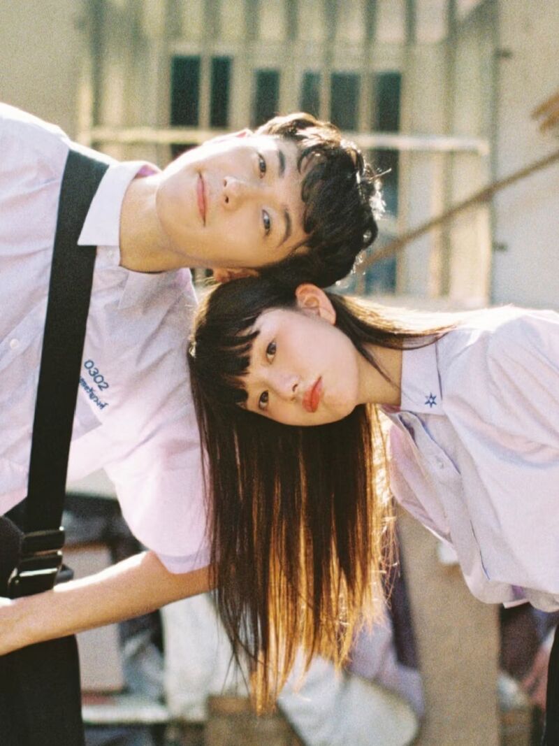 คู่รักหนุ่มสาวในชุดนักเรียนไทยเอียงศีรษะชิดกันในแสงบ่ายสีอุ่น